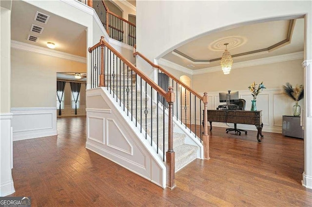 stairs with a tray ceiling, crown molding, and wood-type flooring