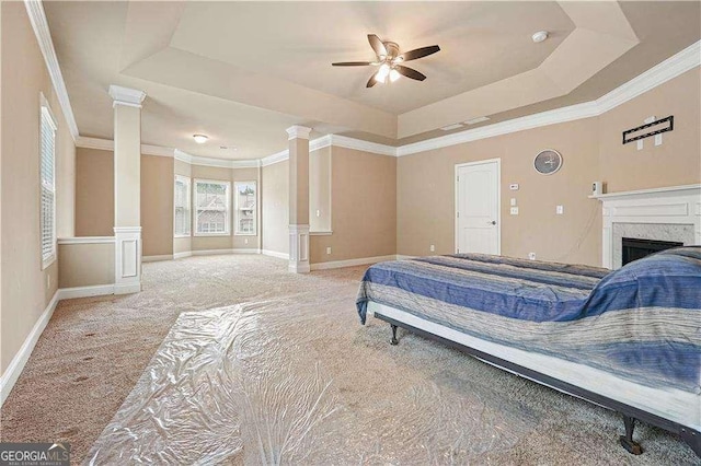 carpeted bedroom with ceiling fan, a raised ceiling, a premium fireplace, decorative columns, and crown molding