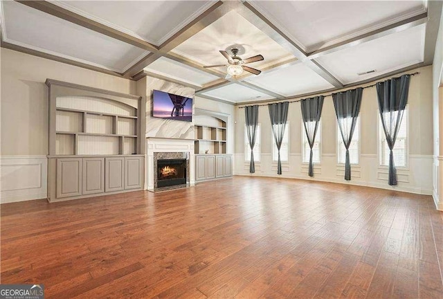 unfurnished living room with hardwood / wood-style floors, coffered ceiling, a premium fireplace, built in features, and beamed ceiling