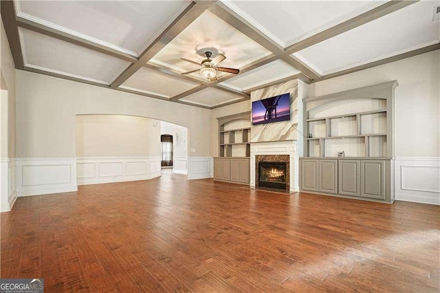 unfurnished living room with a high end fireplace, coffered ceiling, ceiling fan, built in features, and beamed ceiling