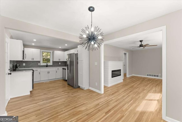 kitchen featuring ceiling fan with notable chandelier, appliances with stainless steel finishes, white cabinetry, tasteful backsplash, and decorative light fixtures