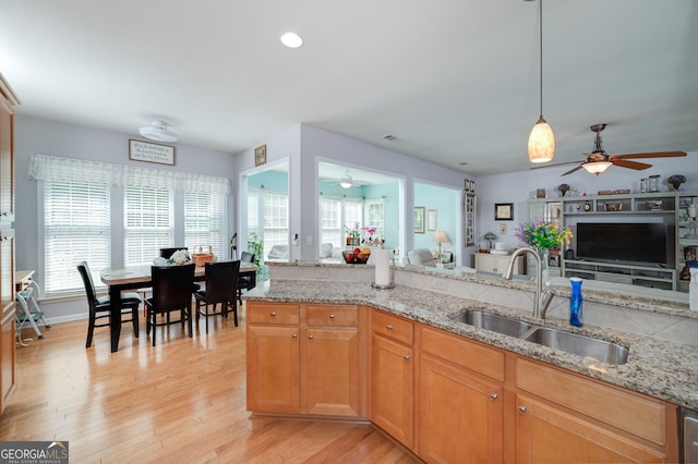 kitchen featuring light stone countertops, sink, ceiling fan, hanging light fixtures, and light hardwood / wood-style floors