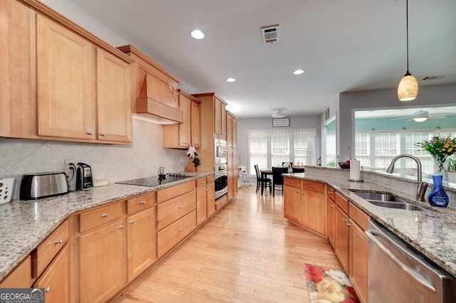 kitchen with custom exhaust hood, sink, hanging light fixtures, light stone countertops, and stainless steel appliances