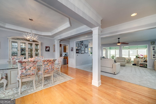 dining room featuring ornate columns, ceiling fan with notable chandelier, a tray ceiling, crown molding, and light hardwood / wood-style flooring