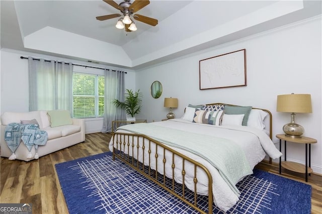 bedroom featuring vaulted ceiling, a raised ceiling, wood finished floors, ceiling fan, and ornamental molding