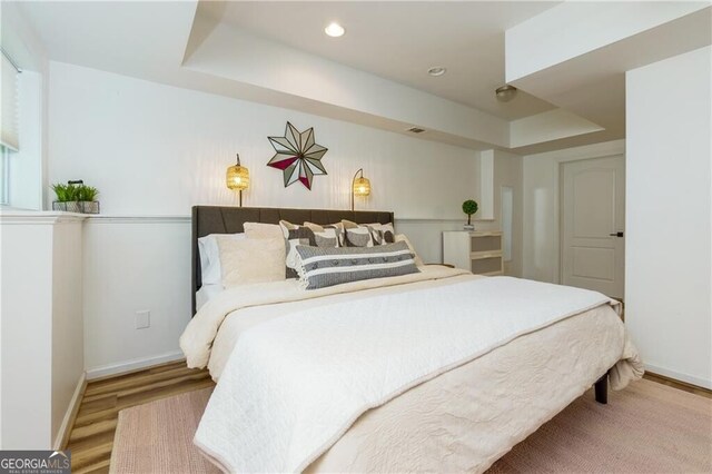 bedroom with a tray ceiling and wood-type flooring