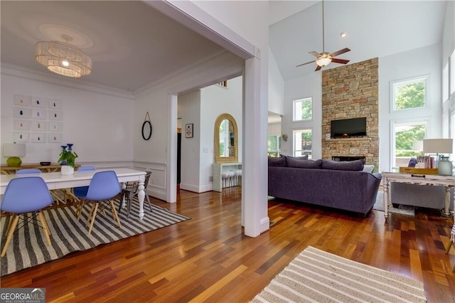 dining area featuring a stone fireplace, ceiling fan, a towering ceiling, and wood-type flooring