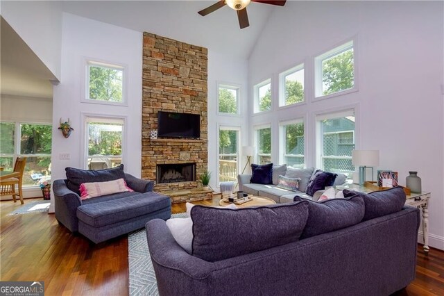 living room with dark hardwood / wood-style flooring, ceiling fan, a fireplace, and a towering ceiling