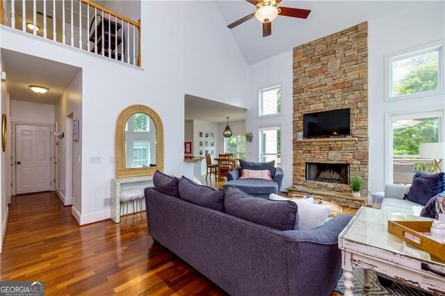 living room featuring ceiling fan, a fireplace, a healthy amount of sunlight, and a high ceiling