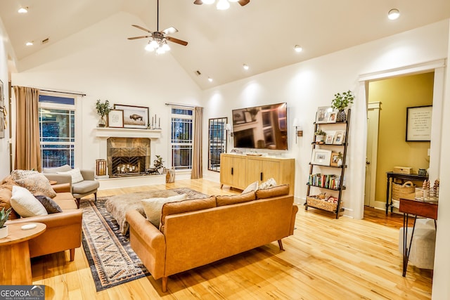 living room featuring ceiling fan, a high end fireplace, high vaulted ceiling, and light hardwood / wood-style flooring