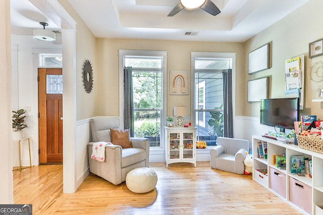 living area with light hardwood / wood-style flooring, ceiling fan, and a tray ceiling