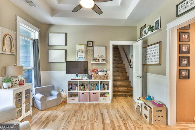 game room with ceiling fan, a tray ceiling, and light wood-type flooring