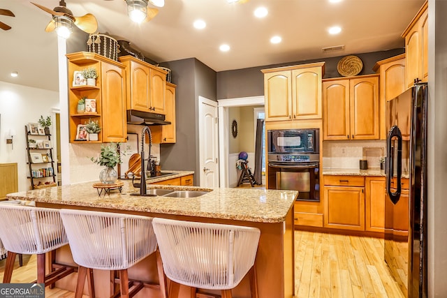 kitchen with a breakfast bar, black appliances, light hardwood / wood-style floors, kitchen peninsula, and light stone countertops