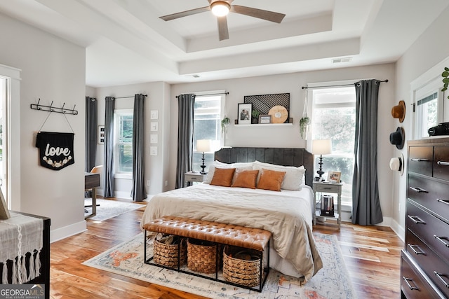 bedroom with ceiling fan, a tray ceiling, and light wood-type flooring