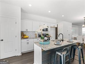 kitchen with a kitchen bar, light stone counters, white cabinetry, and an island with sink