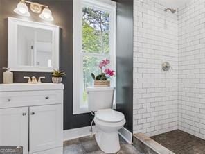 bathroom with toilet, a tile shower, and vanity