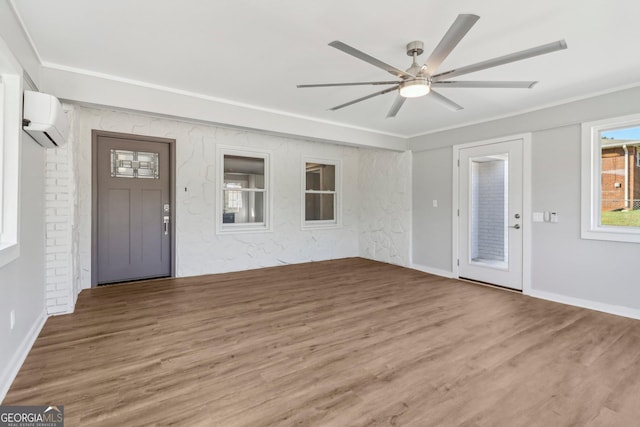 entrance foyer featuring a wall unit AC, ceiling fan, wood-type flooring, and ornamental molding