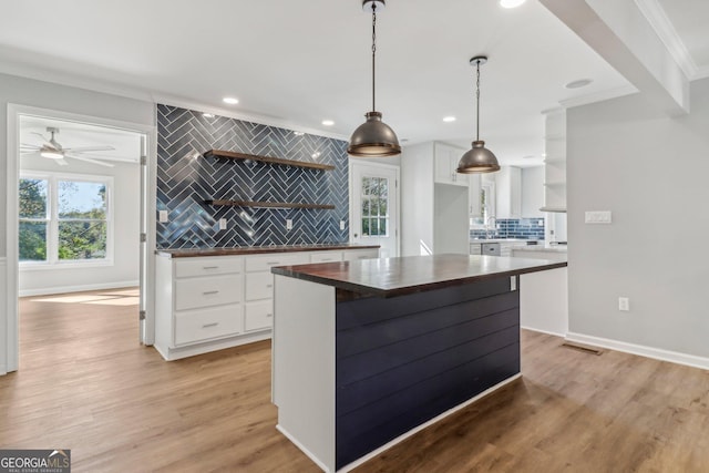 kitchen with wood counters, light hardwood / wood-style floors, pendant lighting, decorative backsplash, and white cabinets