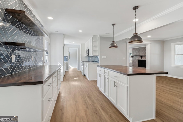 kitchen featuring white cabinetry, hanging light fixtures, backsplash, a kitchen island, and light wood-type flooring