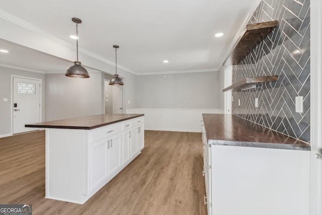 kitchen with light wood-type flooring, crown molding, pendant lighting, white cabinets, and a center island