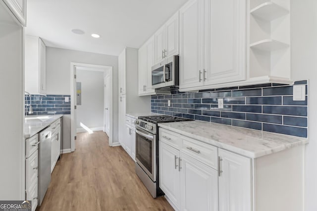 kitchen with light stone counters, white cabinets, stainless steel appliances, and light wood-type flooring