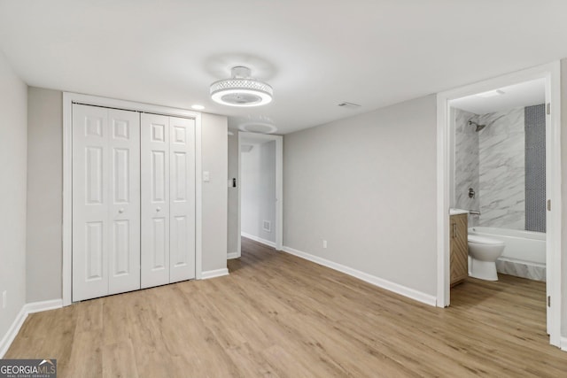 unfurnished bedroom featuring ensuite bathroom, light hardwood / wood-style flooring, and a closet