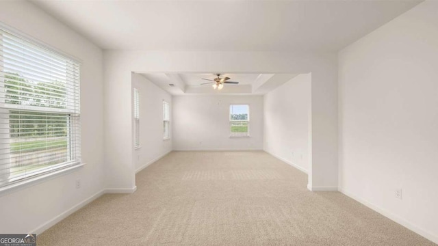 unfurnished room with ceiling fan, light colored carpet, and a tray ceiling