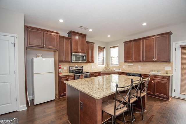 kitchen featuring appliances with stainless steel finishes, a kitchen island, dark wood-type flooring, and a breakfast bar area