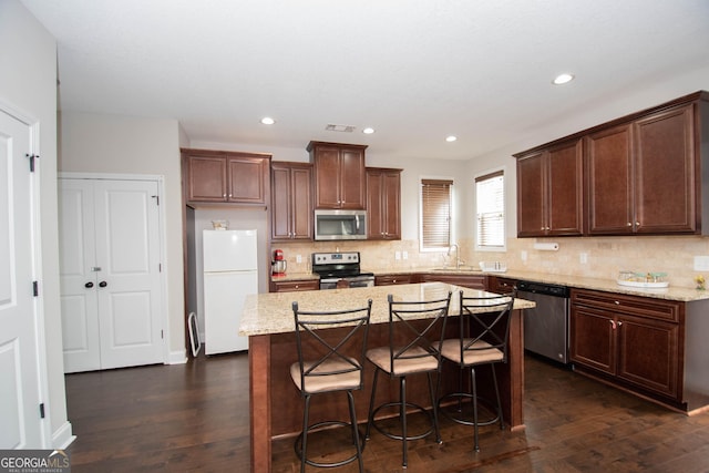 kitchen with dark wood-type flooring, sink, a kitchen island, a kitchen bar, and stainless steel appliances