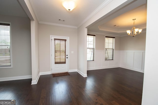 entryway with a raised ceiling, an inviting chandelier, dark wood-type flooring, and ornamental molding