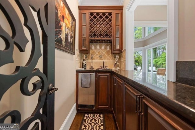 bar featuring dark stone counters, tasteful backsplash, dark hardwood / wood-style floors, and ornamental molding