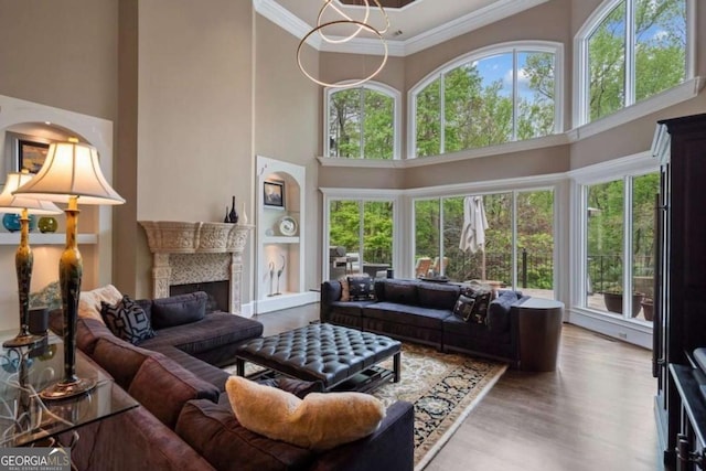 living room with light wood-type flooring, a towering ceiling, a chandelier, and ornamental molding