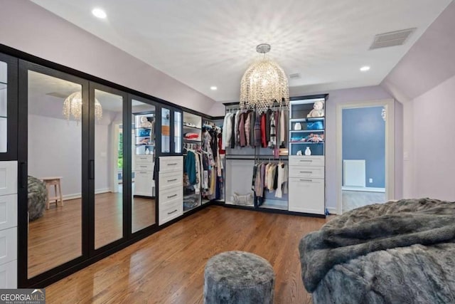 walk in closet with dark hardwood / wood-style floors, vaulted ceiling, and an inviting chandelier