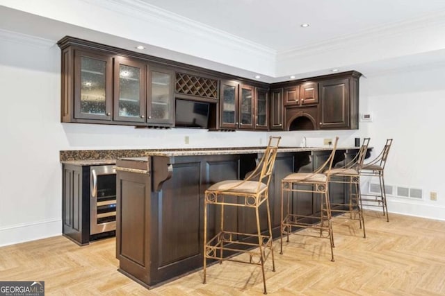 bar with dark brown cabinets, light parquet floors, beverage cooler, and ornamental molding