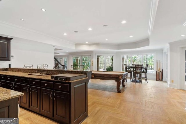 kitchen featuring a tray ceiling, light parquet floors, stone countertops, a center island, and pool table