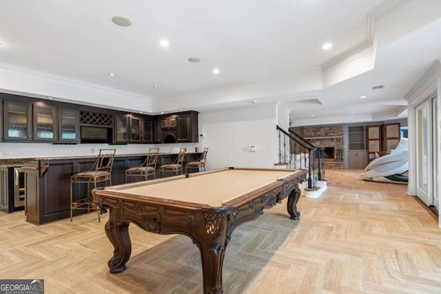 playroom featuring light parquet floors, a stone fireplace, crown molding, pool table, and bar