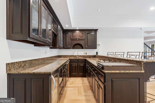 kitchen with dark stone counters, ornamental molding, a breakfast bar, dark brown cabinets, and light parquet floors