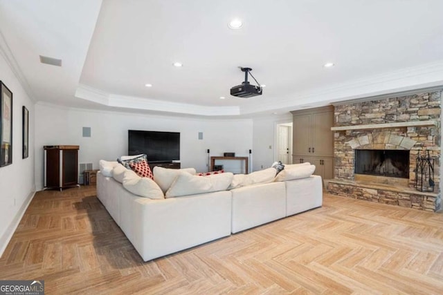 living room with a stone fireplace, a raised ceiling, ornamental molding, and light parquet flooring