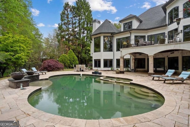 rear view of house featuring a swimming pool with hot tub, a balcony, and a patio