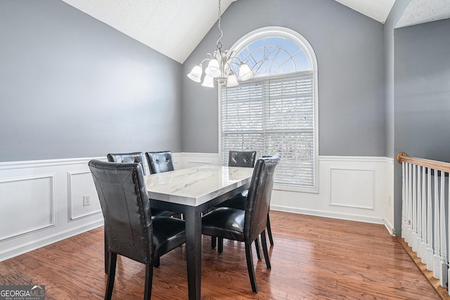 dining area featuring a textured ceiling, wood-type flooring, vaulted ceiling, and an inviting chandelier