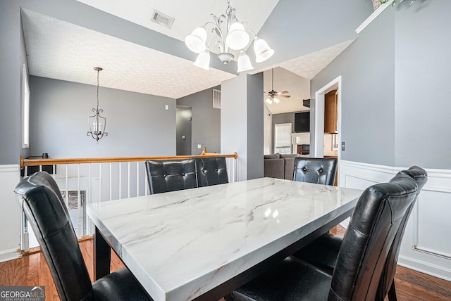 dining space featuring a textured ceiling, ceiling fan with notable chandelier, dark hardwood / wood-style floors, and vaulted ceiling