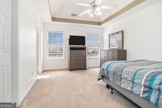 bedroom featuring a textured ceiling, ceiling fan, light carpet, and a tray ceiling