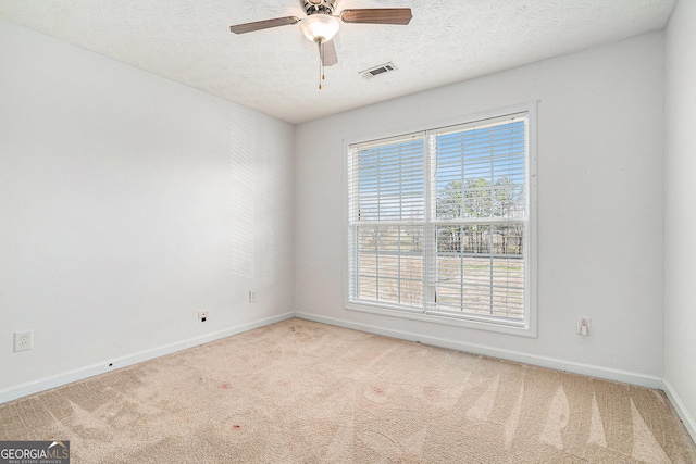 spare room with a textured ceiling, light colored carpet, and ceiling fan