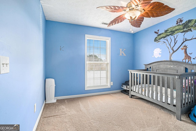 carpeted bedroom with ceiling fan, a textured ceiling, and a nursery area