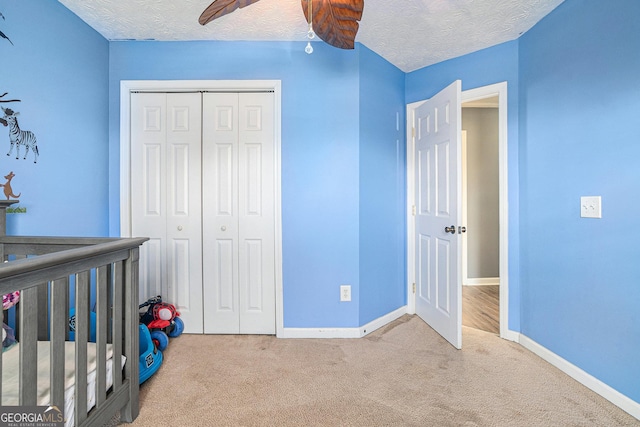 unfurnished bedroom featuring ceiling fan, a textured ceiling, a nursery area, light colored carpet, and a closet