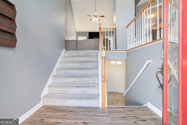 stairs with ceiling fan, wood-type flooring, and a high ceiling