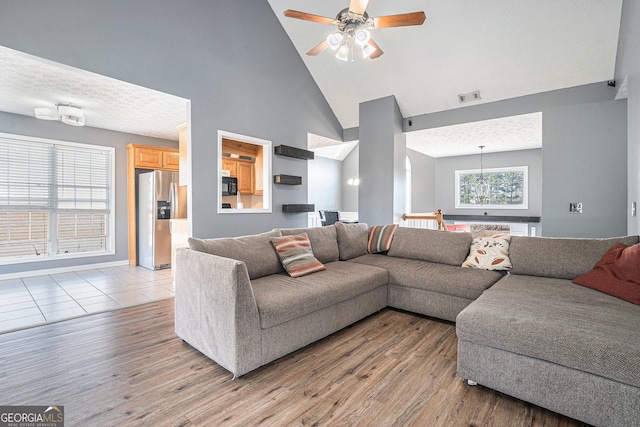 living room with a textured ceiling, light wood-type flooring, high vaulted ceiling, and ceiling fan