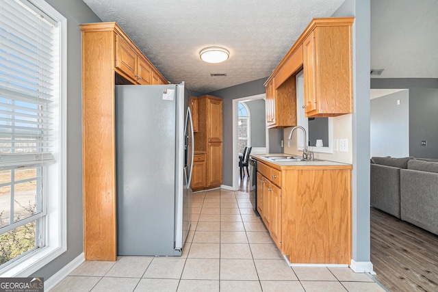 kitchen with a textured ceiling, light tile patterned flooring, sink, and stainless steel refrigerator