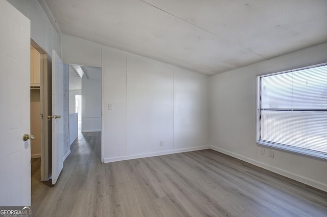 unfurnished room with vaulted ceiling and light wood-type flooring