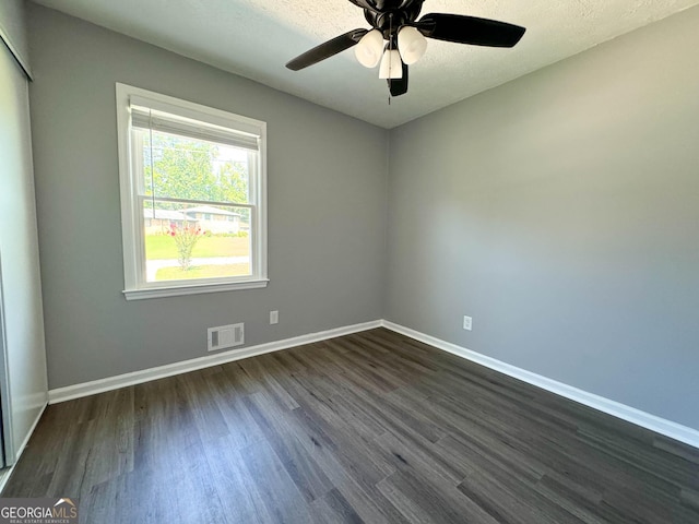 empty room with ceiling fan, dark wood-type flooring, and a textured ceiling